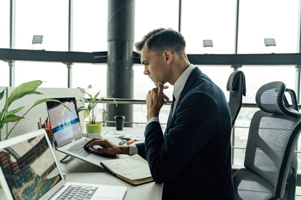 Professional man analyzing stock market data at modern office workspace with laptops.