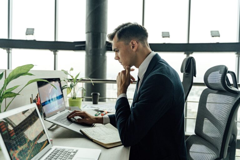 Professional man analyzing stock market data at modern office workspace with laptops.